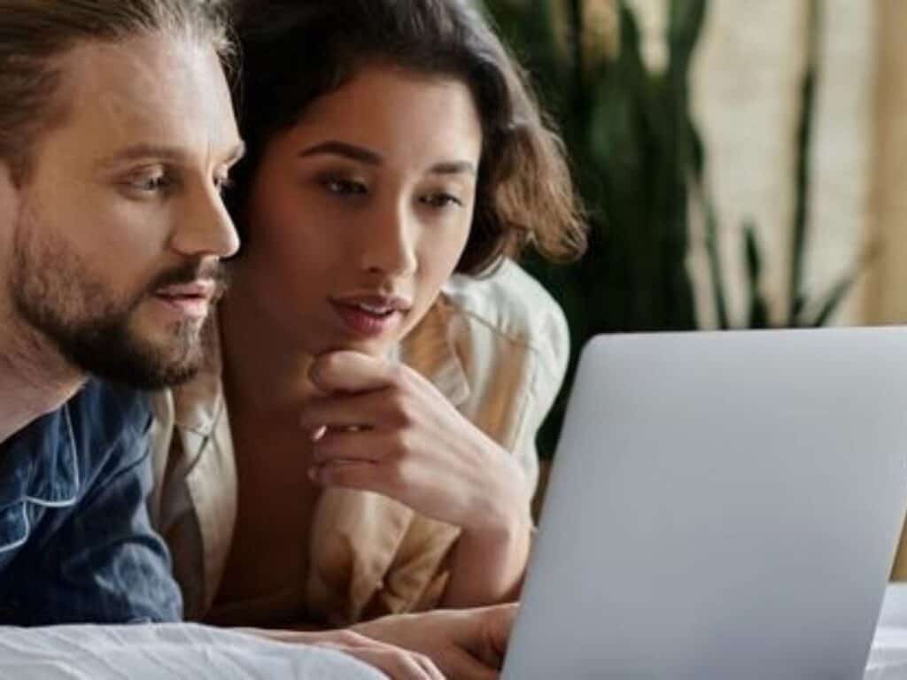 A man and woman couple look at laptop screen, creating their house sitter profile